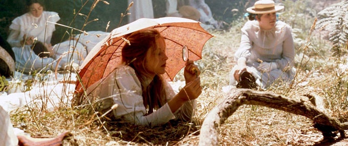 Still from 'Picnic at Hanging Rock' (1975). Girl in white long dress with pink umbrella laying in forest.