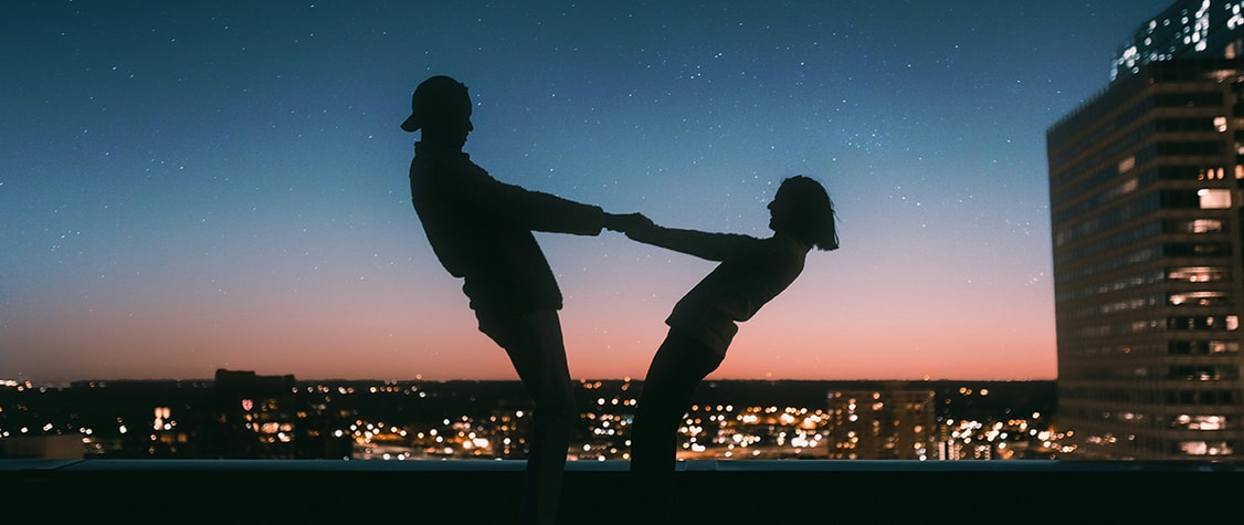 man and woman hold hands on a rooftop beneath the night sky