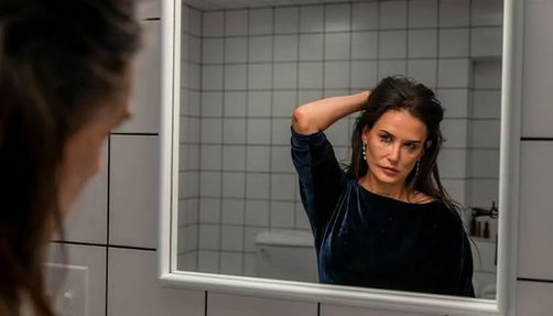 Still from "The Substance" showing Demi Moore looking in a mirror and crying.