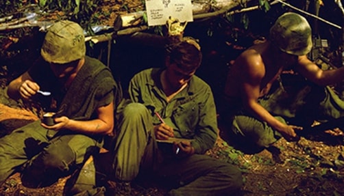 Three American soldiers in Vietnam huddled together.