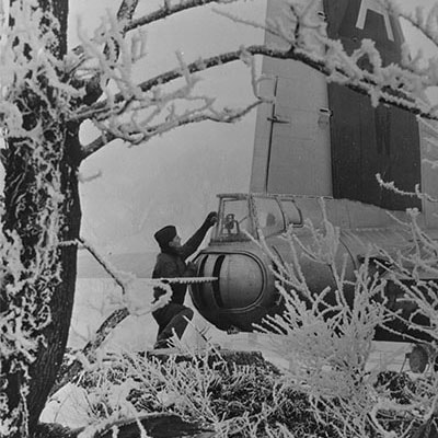A tail gunner of the 91st Bomb Group clears snow from the tail of his B-17 Flying Fortress  - Handwritten caption on reverse: 'Bassingbourn. 48431, OR-W. 91BG. US 8th AF Gunner prepares for take-off - a tail gunner of the 91st Bombardment Group, 8th USAF clears the plexi-glass window in front of his gun sights berfore taking off from a snow shrouded base 'in England'.