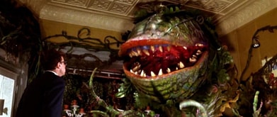 Rick Moranis as Seymour Krelborn, standing across from the monstrous Audrey II plant in 'Little Shop of Horrors.'