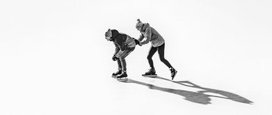 a woman pushes a man forward on ice skates