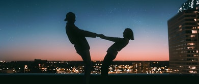 man and woman hold hands on a rooftop beneath the night sky
