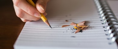 Hand with pencil writing on notebook paper with pencil shavings